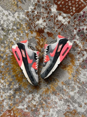 Nike Air Max 90 Infrared sneakers - Nike Air Max 90 sneakers i färgen Infrared med grå, svarta och vita paneler samt röda detaljer. Klassisk låg siluett med synlig Air-enhet i sulan och mesh, mocka och lädermaterial. Ikonisk Swoosh på sidan och AIR MAX-logga vid hälen.