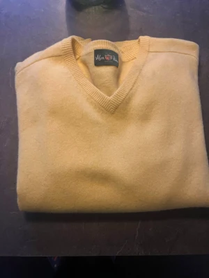 Gul v-ringad stickad tröja Alan Paine - Snygg gul stickad tröja från Alan Paine  med v-ringad hals och ribbade muddar. Tröjan har en enkel och klassisk design som passar perfekt till jeans eller kjol. Tillverkad i mjukt material för en bekväm känsla.