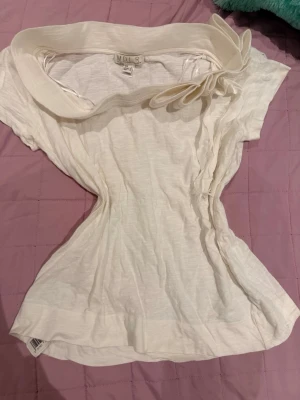 Vit blus med stor krage och blomdetalj - Säljer en vit blus från MOR med stor, dekorativ krage och en unik blomdetalj på axeln. Blusen har korta ärmar och är tillverkad i ett tunt, mjukt material som känns luftigt. Perfekt för dig som gillar statement-detaljer och en feminin look.