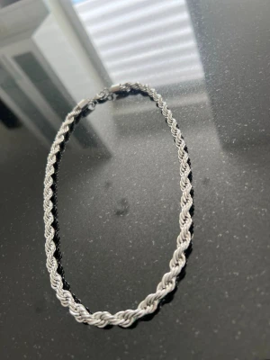 Cordell Halsband 7mm - Säljer ett snyggt halsband med tvinnad kedja i silverfärg. Halsbandet har en klassisk karbinlås och är tillverkat i metall. Perfekt för dig som gillar stilrena accessoarer med lite extra detalj. Passar till många olika outfits.