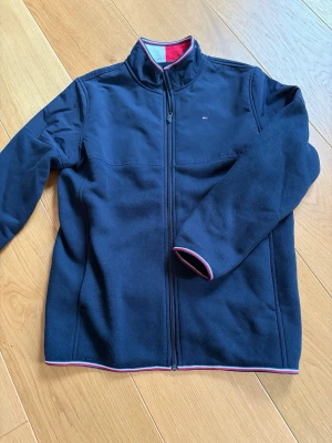 Marinblå fleecejacka Tommy Hilfiger - Snygg marinblå fleecejacka från Tommy Hilfiger med hel dragkedja och hög krage. Väldigt bra skick storlek 16-18! Skriv vid frågor!