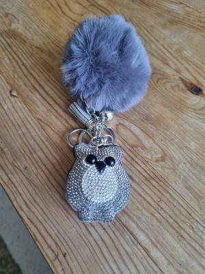 Nyckelring med uggla och fluffboll - Säljer en snygg nyckelring med en glittrig uggla i silver och en stor grå fluffboll. Ugglan är dekorerad med små stenar och har svarta ögon. Perfekt som accessoar till väskan eller nycklarna.