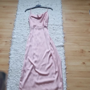 Ljusrosa långklänning i satin - Supersnygg ljusrosa långklänning i glansigt satinmaterial. Klänningen har smala axelband, lätt draperad urringning och en elegant, figurnära passform. Perfekt för dig som vill ha en stilren och trendig look. Storlek 38 men är ganska liten för storleken. Aldrig andvänt då jag valde ha en annan klänning på min bal❤️