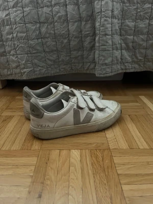 Vita Veja sneakers - Snygga vita sneakers från Veja med beige detaljer och kardborreband istället för snörning. Skorna har låg profil och är tillverkade i läder med textilfoder. Perfekta för en clean och stilren look.