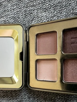 Hourglass ögonskuggspalett i guld - Snygg ögonskuggspalett från Hourglass i en lyxig guldfärgad metallask. Paletten innehåller fyra nyanser: två ljusa nude och två mörkare bruna toner, perfekta för att skapa både mjuka och intensiva ögonlooks. Kompakt format med spegel i locket.