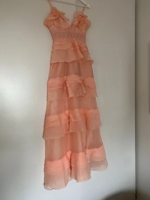 Sophia Soft Peach balklänning  - Oanvänd. Köpte två likadana i olika storlekar och använde den andra på studentbalen. Har upptäckt ett miniminihål på ena volangen, se bild.