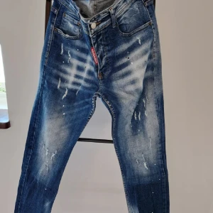 Blå jeans med slitningar från Dsquared2 - Snygga blå jeans från Dsquared2 med coola slitningar och en ikonisk logga på baksidan. De har en klassisk femficksdesign och knappgylf. Perfekta för en trendig look!
