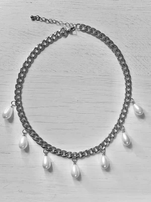 Kedjehalsband med droppformade pärlor - Snyggt halsband med grov silverfärgad kedja och sju droppformade vita pärlor som hänger längs kedjan. Perfekt för att ge en cool och trendig touch till din outfit. Justerbar längd med karbinlås.