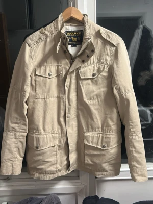 Beige Fieldjacket från Woolrich - Fieldjacket från Woolrich i nyskick. Populär modell. Storlek Medium. Pris 899. Skriv vid funderingar!🙌