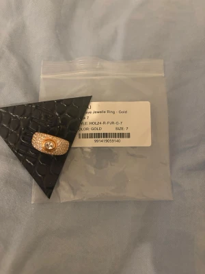 Guldpleterad ring med stenar - Snygg guldfärgad ring med glittrande stenar runt hela bandet och en större klar sten i mitten. Ringen har en modern och lyxig känsla, perfekt för att lyfta din stil. Storlek 7.