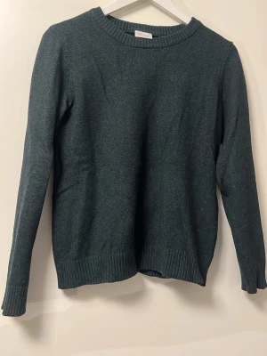 Mörkgrön stickad tröja vila - En enkel och stilren mörkgrön finstickad tröja med rund halsringning och ribbade muddar vid ärmslut och nederkant. Perfekt för lager på lager och passar till det mesta. Tröjan har en klassisk passform och är gjord i mjukt material som inte sticks.