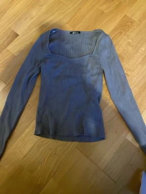 Gråribbad topp från Gina Tricot - Trendig grå topp från Gina Tricot med ribbad struktur och lång ärm. Toppen har en snygg, något djupare urringning och sitter figurnära. Perfekt att styla med jeans eller kjol för en cool look.