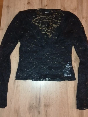 Svart spetsblus med v-ringning - Snygg svart blus från Bik Bok i transparent spets med v-ringning och långa ärmar. Perfekt att styla med jeans eller kjol för en trendig look. Blusen har en figurnära passform och är riktigt bekväm.