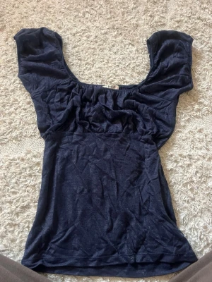 Mörkblå topp med puffärmar - Trendig mörkblå topp med bred urringning och puffiga korta ärmar. Tunn och mjuk i materialet, perfekt för att styla med jeans eller kjol. Enkel men ändå snygg design❣️
