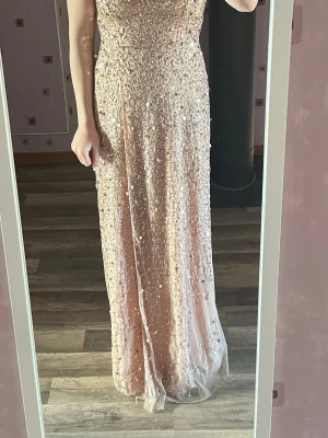  paljettbalklänning - Säljer en magisk balklänning i ljusrosa med massor av paljetter som ger ett riktigt glittrigt intryck. Klänningen har figurnära passform upptill och faller snyggt längs kroppen. Perfekt för bal eller festkvällar där du vill glänsa extra mycket.