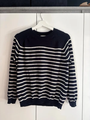 Marinblåvit randig stickad tröja - Stickad tröja i marinblått med vita horisontella ränder. Tröjan har rund halsringning, långa ärmar och ribbstickade muddar vid ärmslut och nederkant. Perfekt för en avslappnad och stilren look. 100% kaschmir.