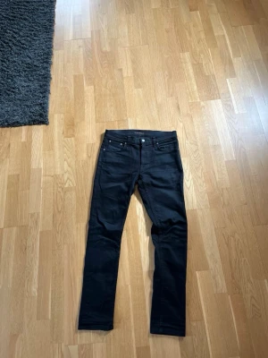 Svarta skinny Nudie jeans - Säljer ett par svarta skinny Nudie jeans med klassisk femficksdesign och smal passform. Jeansen har normal midja och är tillverkade i ett stretchigt material som sitter snyggt. Perfekta för dig som gillar en clean och stilren look.