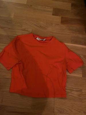 Röd croppad t-shirt från Weekday - Snygg röd t-shirt från Weekday med croppad passform och klassisk rund hals. Tillverkad i mjuk bomull och har korta ärmar. Perfekt för dig som gillar enkel men trendig stil.