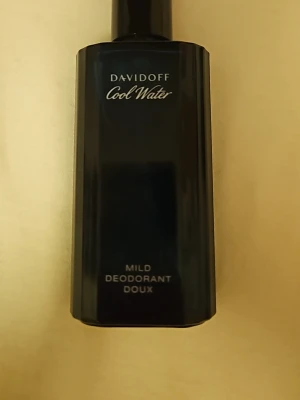 Davidoff Cool Water Mild Deodorant - Davidoff Cool Water Mild Deodorant är en elegant parfym i en mörkblå, rektangulär glasflaska med svart lock. Flaskan rymmer 75 ml och har en stilren design med vita tryckta detaljer. Perfekt för dig som gillar fräscha och klassiska dofter.
