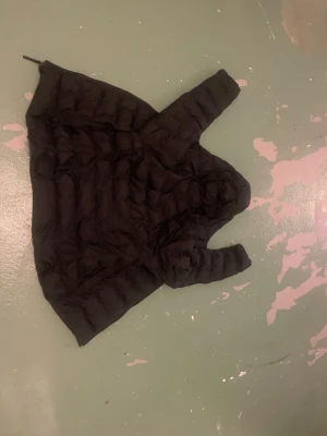 Svart dunjacka med huva - Säljer en svart dunjacka med huva och quiltad design. Jackan har en klassisk puffer-look och dragkedja framtill. Perfekt för kalla vinterdagar och riktigt skön att bära. Passar dig som vill ha en enkel men snygg vinterjacka.