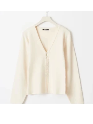 Krämvit kofta med knappar GINA  - Stilren krämvit kofta med v-ringning och dekorativa knappar framtill. Koftan har lång ärm och rak passform, perfekt att matcha med olika outfits. Tillverkad i mjukt stickat material för en bekväm känsla.