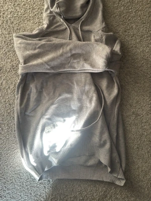 Grå hoodie med huva och ficka - En enkel grå hoodie med klassisk huva och stor magficka. Tröjan har ribbade muddar vid ärmslut och nederkant, och är gjord i mjukt bomullsmaterial. Perfekt för att chilla eller hänga med kompisar.