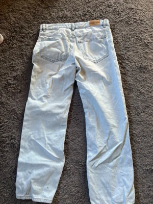 Ljusblå raka jeans - Säljer ett par ljusblå jeans med rak passform och klassisk femficksdesign. Jeansen har bälteshällor och en patch bak i midjan. Perfekta för en avslappnad och trendig look. Materialet är denim i bomull.