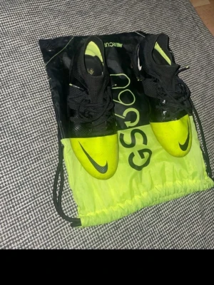 Nike Mercurial GS360 fotbollsskor - Säljer ett par Nike Mercurial GS360 fotbollsskor i svart och neon-gult. Skorna har en strömlinjeformad design med snörning och Nike-logga på tån. Ovandelen är i syntetmaterial för bra grepp och känsla på planen. Perfekta för dig som vill sticka ut på fotbollsplanen.