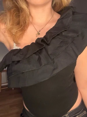 Jätte eftertraktad Zara volangbody i svart  - Säljer en svart body från Zara med stora volangdetaljer över axeln. Den är snygg och har en asymmetrisk design som verkligen sticker ut. Perfekt för dig som vill ha något unikt och trendigt i garderoben. Den är i storlek M men skulle säga passar en storlek S bättre. Passar mig och jag har alltid XS/S. 