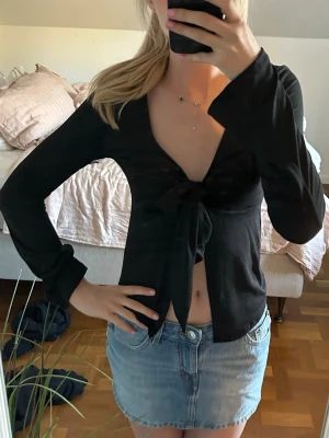 Svart omlottopp med knyt framtill - Svart topp med långa ärmar och djup v-ringning. Toppen har ett snyggt knyt framtill.