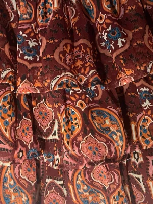 Mönstrad populär kortkjol i boho-stil - Säljer en kortkjol med bohemiskt paisleymönster i vinröda, orangea och blå toner. Väldigt populär kjol! Kjolen har volangdetaljer och är tillverkad i ett lätt, flödande tyg som ger en skön och avslappnad känsla. Perfekt för dig som gillar färg och mönster! Storlek 146/152 men passar mig som 172. Den är väldigt stretchig i midjan och blir inte för kort för mig. Endast andvänd få gånger och inga tecken på slitage