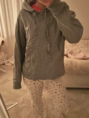 Grå hoodie från Acne Studios - Säljer en grå hoodie från Acne Studios med klassisk känguruficka och dragsko i huvan. Hoodien har en liten patch med logga på bröstet och är gjord i mjukt bomullsmaterial. Perfekt för en chill och avslappnad stil.