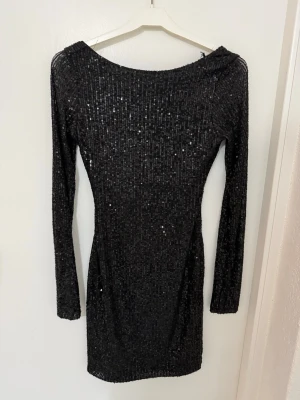 Svart glittrig paljettklänning - Snygg svart kortklänning med långa ärmar och öppen rygg. Klänningen är täckt av glittriga paljetter och har en tight passform som framhäver figuren. Perfekt för dig som vill sticka ut på nästa fest! Materialet känns stretchigt och bekvämt. (Egna bilder) skriv till mig vid frågor💕💕 kan kolla upp vart jag köpt klänningen om det skulle behövas!