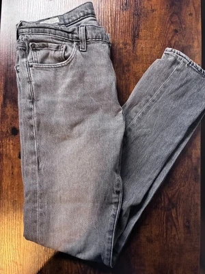 Grå Levi's Premium raka jeans - Säljer ett par grå Levi's Premium jeans med rak passform och klassisk femficksdesign. Jeansen är tillverkade i bomull och har en snygg vintagekänsla. Perfekta för dig som gillar en avslappnad men stilren look.