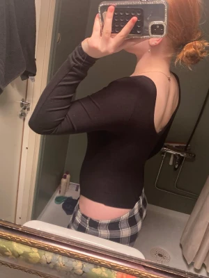 Svart långärmad body med djup rygg - Säljer en svart body med långa ärmar och djup, rundad rygg. Bodyn har en tight passform och är tillverkad i ett stretchigt material som sitter snyggt mot kroppen. Perfekt att styla med jeans eller kjol för en clean look.