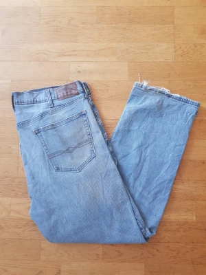 Levi's Denizen  - Säljer ett par ljusblå raka jeans från Levi's Denizen med klassisk femficksdesign och rå kant nedtill. Jeansen har en avslappnad passform och är tillverkade i slitstark denim. Perfekta för en casual och trendig look.