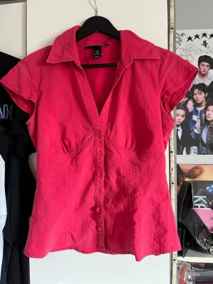 Rosa kortärmad blus med knappar - Snygg rosa blus från H&M med korta ärmar och klassisk krage. Blusen har knappar framtill och en figurnära passform som ger en feminin siluett. Tillverkad i ett lätt, strukturerat tyg som känns bekvämt och luftigt.