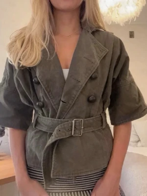 Grön vårjacka  med bälte och knappar -  grön vårjacka  med breda trekvartsärmar, dubbelknäppning och matchande bälte i midjan. 