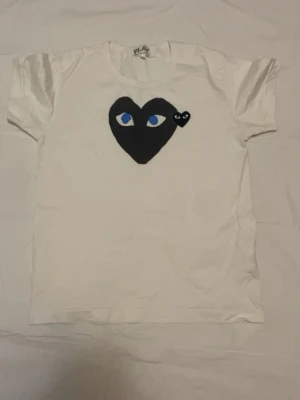 Vit Comme des Garçons PLAY t-shirt - Säljer en vit t-shirt från Comme des Garçons PLAY med det ikoniska svarta hjärtat med blå ögon tryckt på bröstet och en liten svart hjärtdetalj bredvid. Klassisk rund hals och korta ärmar. Pris kan diskuteras vid snabbaffär. Tveka på att ställa frågor 