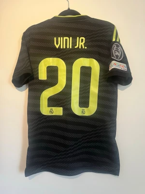 Original real madrid 2022/23 tredje tröja vini jr #20 + CL patch adidas - Säljer en väldigt snygg och ovanlig real Madrid fotbollströja! Det är nämligen tredje tröjan från säsongen 2022/23 med den snabba och tekniska storstjärnan vinicius junior nummer 20 på ryggen! Äkta såklart💪.                                                Skick 9/10 i nyskick! Storlek: XS herr passar S Adidas + Champions league patch 14 st  Hör av dig vid minsta lilla fundering o h kolla gärna in mina andra artiklar!