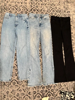 Tre par jeans i olika tvättar - Säljer tre par jeans: två i ljusblå tvätt med raka ben och ett par svarta med utsvängda ben. Alla har klassisk femficksdesign och knappgylf. Perfekta för dig som gillar olika stilar på jeans och vill variera mellan ljusa och mörka färger.