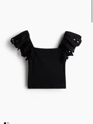 Svart topp med broderade puffärmar - Topp som inte går att få tag i längre!! Supersnygg svart topp med fyrkantig urringning och puffiga kortärmar i broderad bomull med hålmönster. Kroppsdelen är ribbad och stretchig vilket ger en bekväm passform. Perfekt att styla med jeans eller kjol för en trendig look.