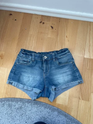 Blå jeansshorts  - Säljer ett par klassiska blå jeansshorts från LAB Industries. De har fem fickor och bälteshällor. Shortsen har en knapp och dragkedja framtill samt en snygg tvättad look. Perfekta för sommaren och riktigt sköna att bära. Storlek 158, skulle säga att de är som xs. 