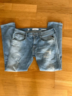 Ljusblå slitna jeans från Replay - Säljer ett par ljusblå jeans från Replay med slitningar och tvättade detaljer. Storlek 33/32. Klassisk femficksmodell med slim fit. Jeansen har snygga slitningar framtill och Replay-logga på bakfickan. Perfekta för en stilren look. 