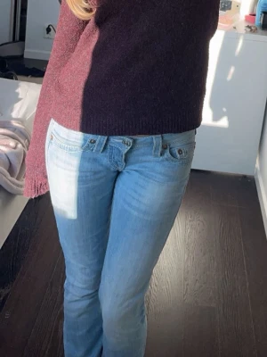 True religion jeans - Säljer ett par ljusblå bootcut jeans med klassisk femficksdesign och låg midja. Jeansen har en snygg tvättad look och är perfekta för en avslappnad stil. Passar dig som gillar en tidlös och enkel vibe.
