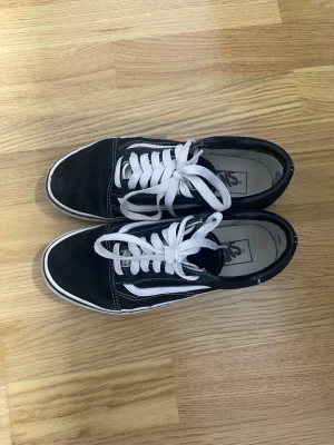 Svarta Vans sneakers - Klassiska Vans sneakers i svart med vit sula och vit sidostripes. Skorna har vita snören och kontrastsömmar som ger en clean och tidlös look. Ovandelen är i mocka och canvas vilket gör dem både snygga och bekväma till vardags.