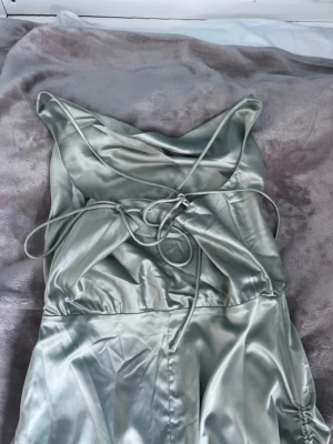 Ljusgrön satin klänning med snörning - Snygg ljusgrön klänning med smala axelband. Klänningen har drapering framtill och justerbara snören på sidorna. Perfekt för firanden.                     Material: Polyester