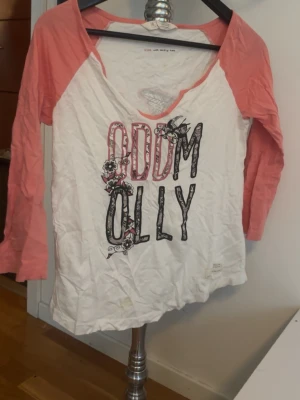 Odd Molly långärmad topp rosa/vit - Snygg långärmad topp från Odd Molly med vita och rosa partier. Tryck med Odd Molly-logga och blommor framtill samt stor fågelgrafik på ryggen. Tillverkad i mjuk bomull och har en avslappnad passform med v-ringad hals.