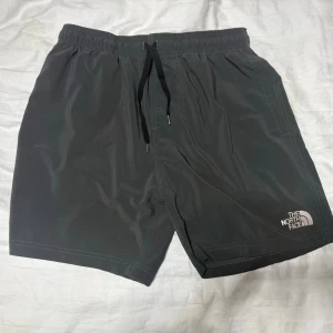 The North Face shorts/badbyxor - Snygga mörkgrå badshorts/shorts från The North Face, perfekta för sommaren. Klassisk logga på vänster ben och två sidofickor. Enkel och stilren design som funkar till det mesta. Helt oanvända!