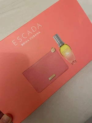 Escada Brisa Cubana parfymset - Snyggt parfymset från Escada med doften Brisa Cubana. Förpackningen är rosa med färgglad kubansk design och innehåller en parfymflaska med silverfärgad kork samt en matchande rosa necessär med metallmärke. Perfekt present till någon som gillar fräscha och tropiska dofter.